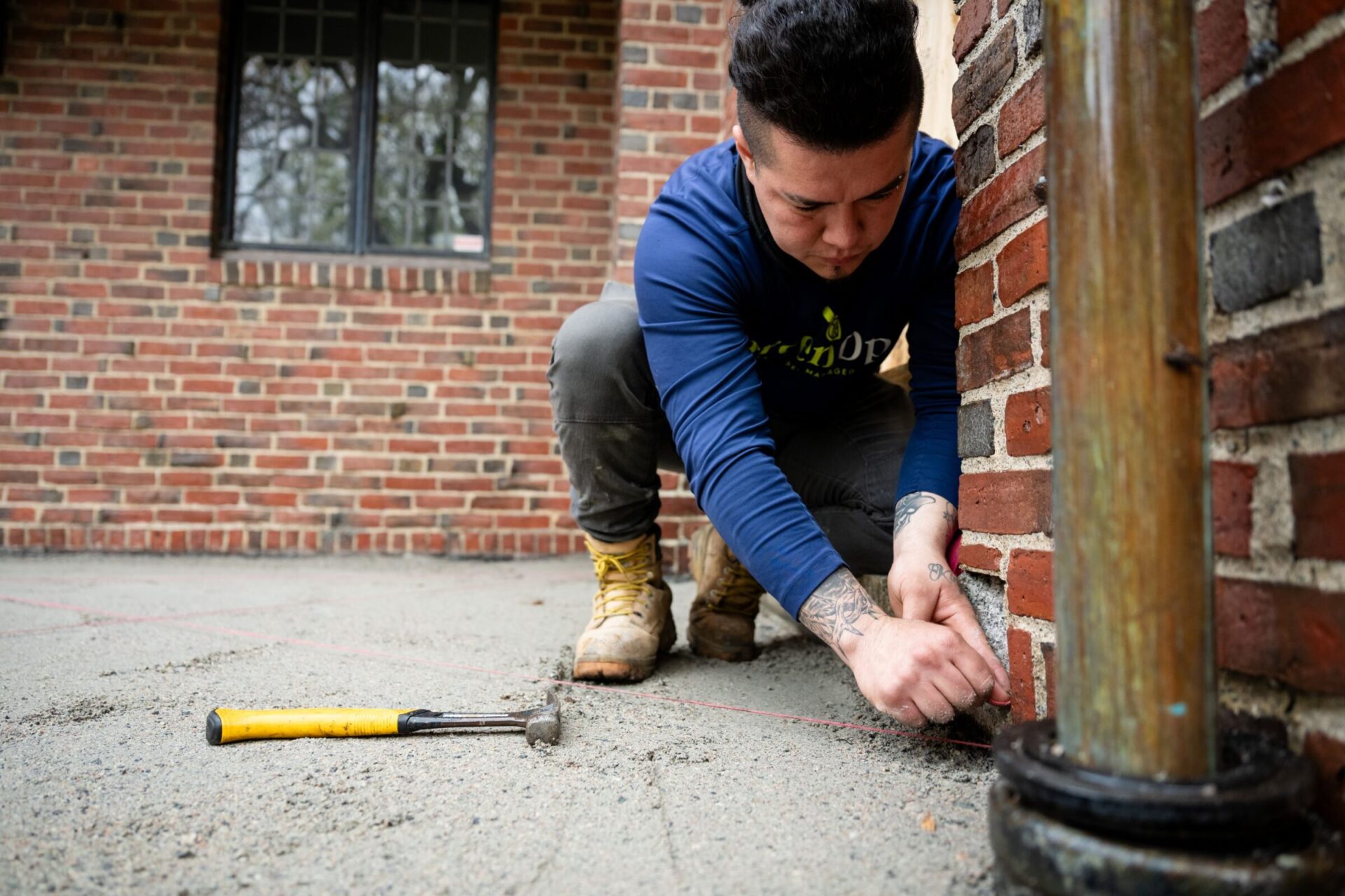 A person working with tools near a brick wall, wearing boots and a blue shirt, focused on precision in construction work.