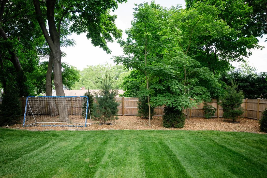 A well-maintained backyard features lush grass, tall trees, a wooden fence, and a small soccer goal, creating a serene outdoor space.