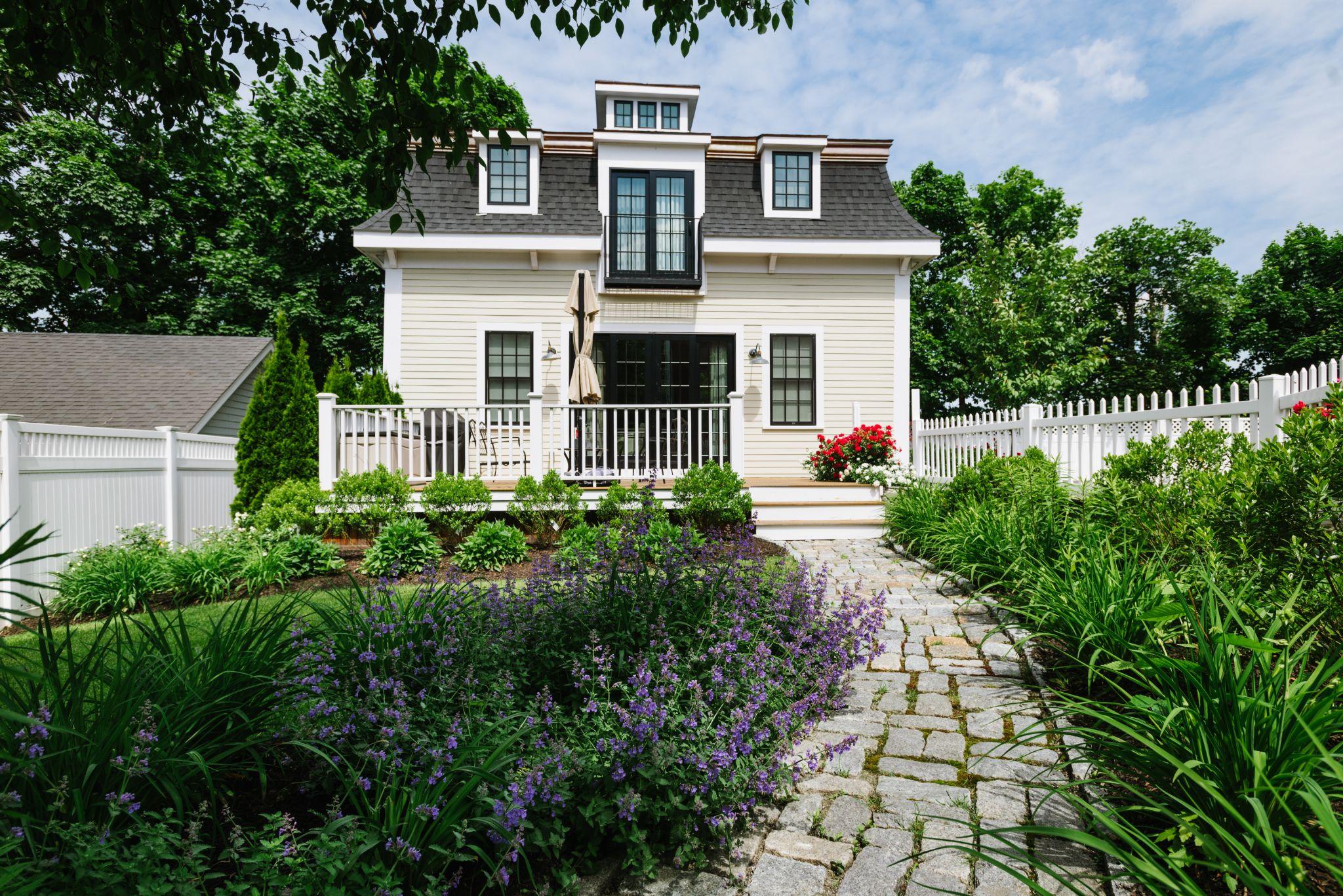 Stone pathway through a lush garden leading to a white cottage-style home.